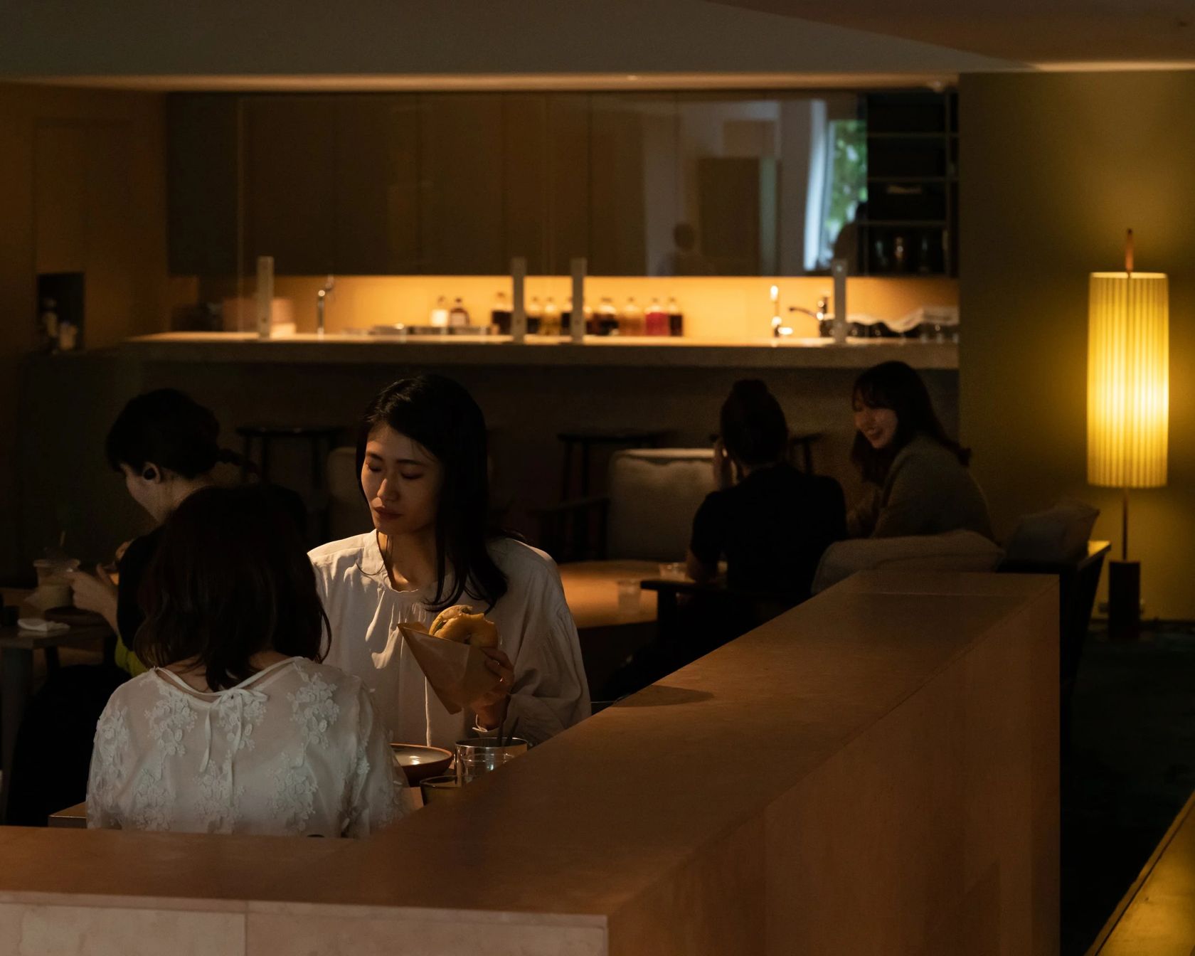 Clientes no ambiente da Abno, com o balcão iluminado ao fundo, no DDD HOTEL, em Tóquio
