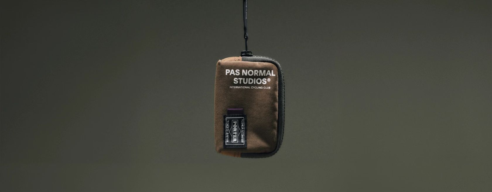 Coin case da collab PORTER e Pas Normal Studios suspenso diante de fundo verde-oliva