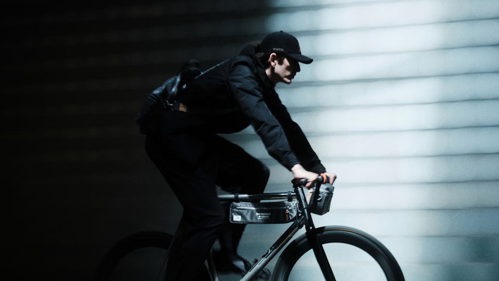 Ciclista da campanha PORTER e Pas Normal Studios pedala com bolsas fixadas à bicicleta em cenário urbano escuro