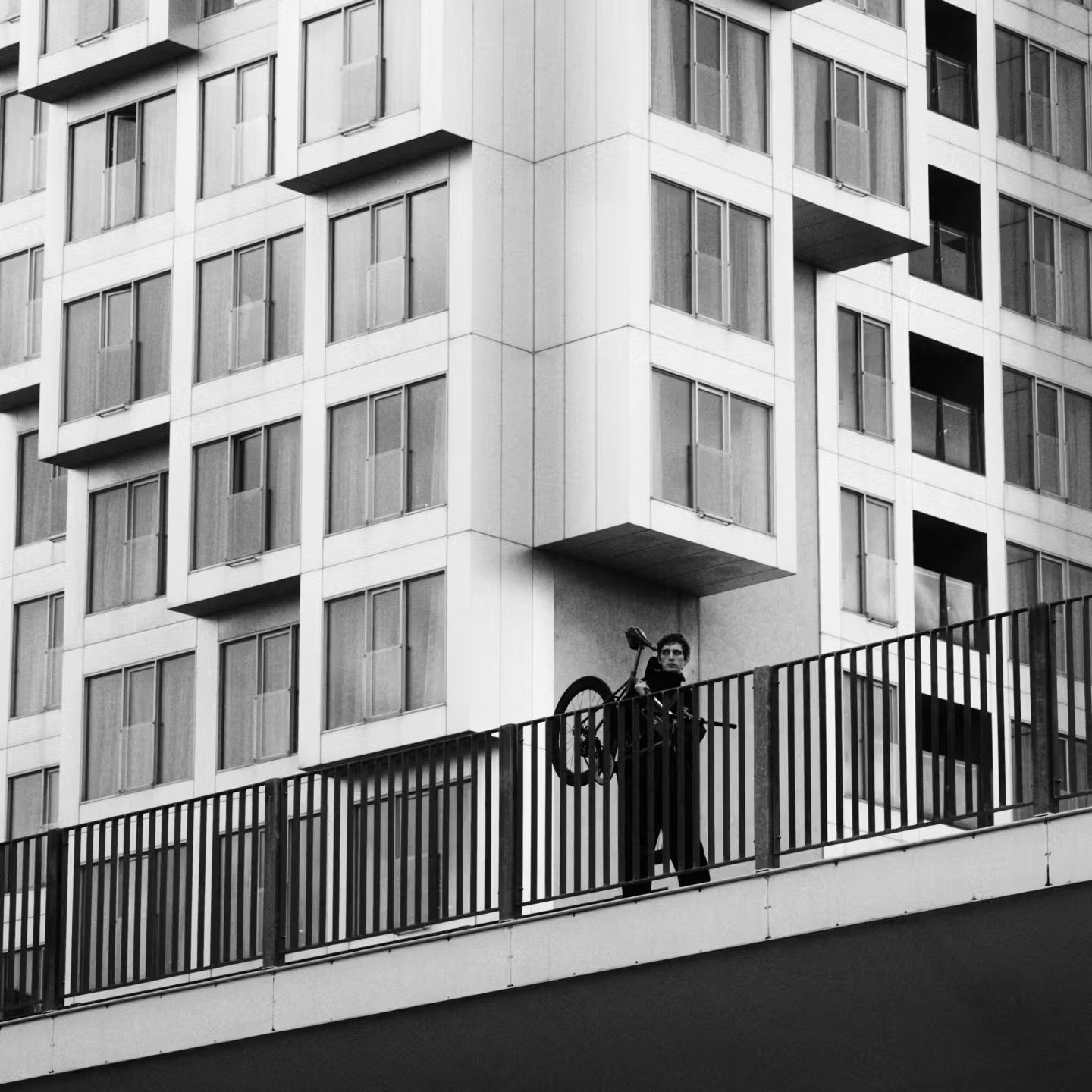 Ciclista carrega a bicicleta diante de edifício geométrico em campanha da parceria PORTER e Pas Normal Studios